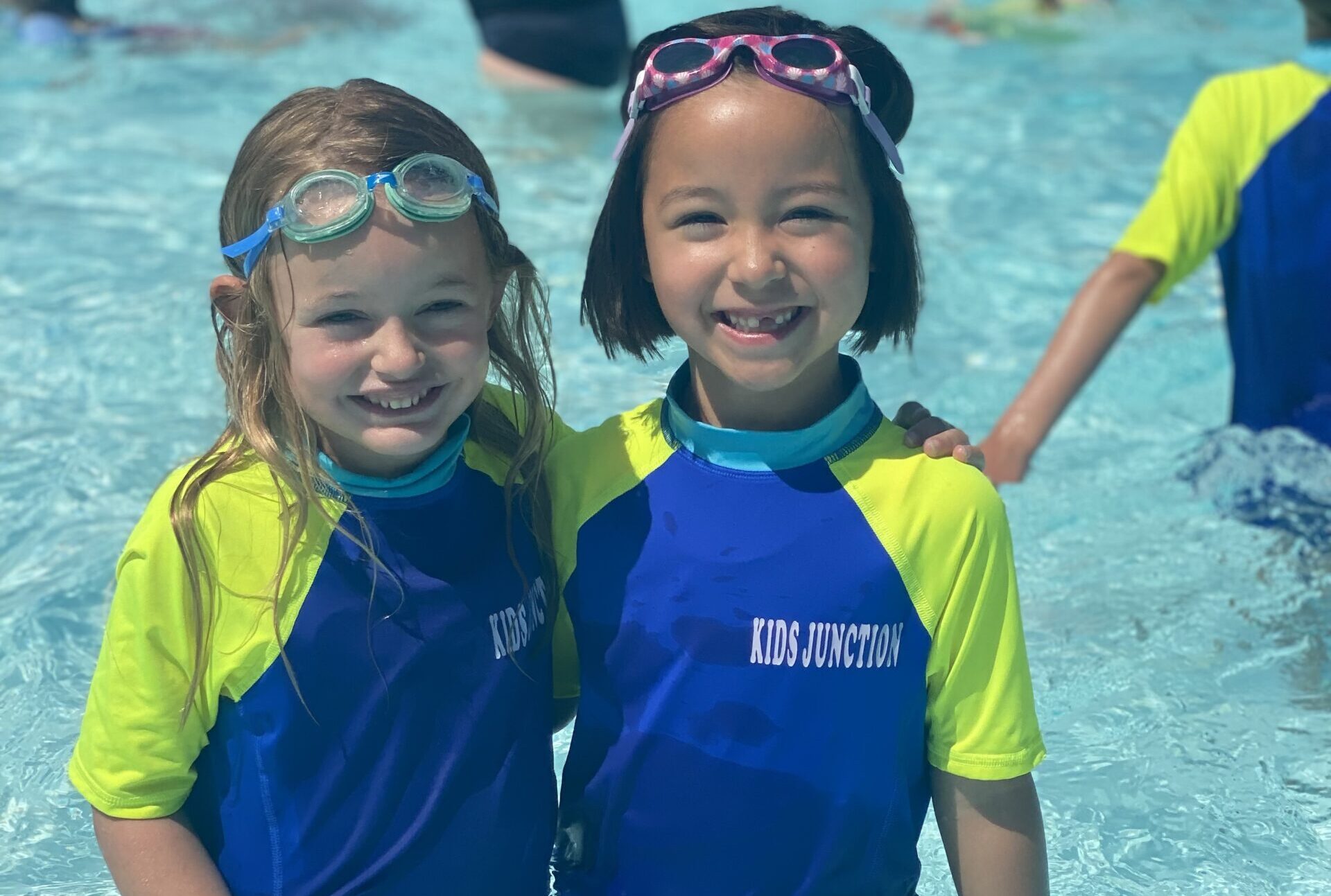 Girls_Summer_Pool_Trip A picture of two little girls in Kids Junction rash guards wearing goggles on their heads and smiling at the camera.