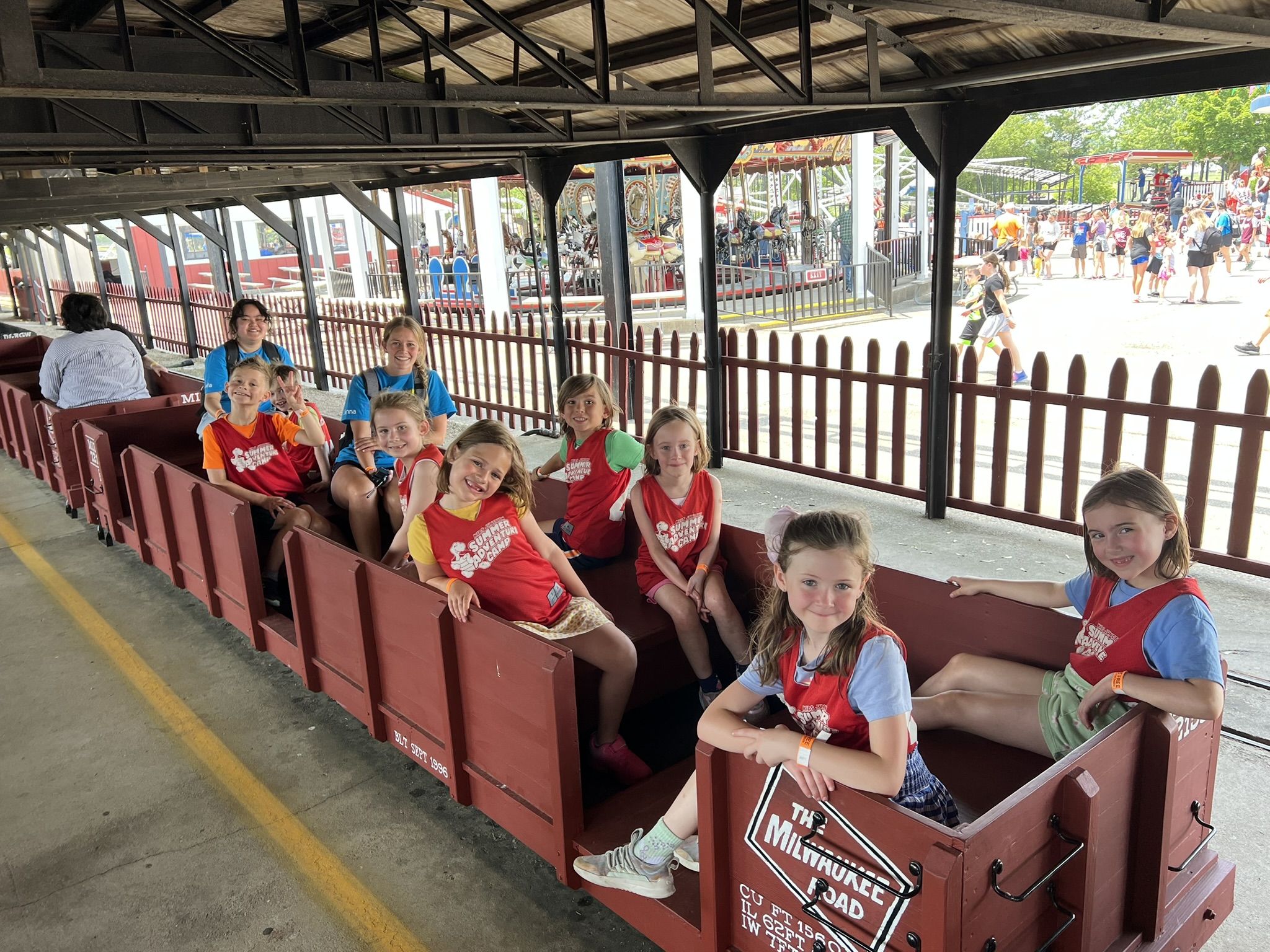 A picture of Summer Adventure Camp campers on a train at Little Amerricka Amusement Park. The campers are wearing their Summer Adventure Camp vests and smiling at the camera.