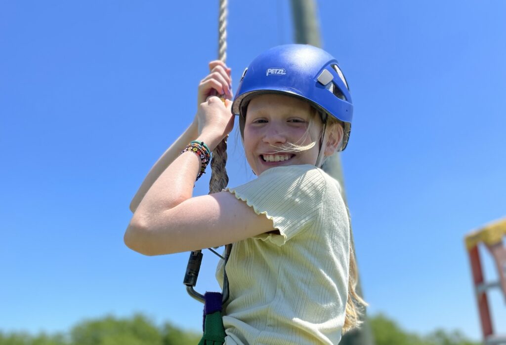 A Summer Adventure Camp Senior camper smiling at the camera as she is on the zipline.